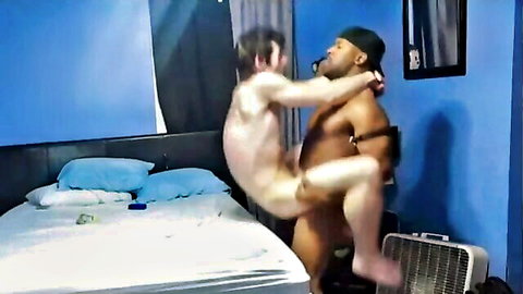 Muscular Black daddy lifts smiling white boy toy in nude embrace