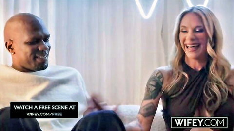 Blonde tattooed wife laughing with smiling black bull on couch at wifey.com