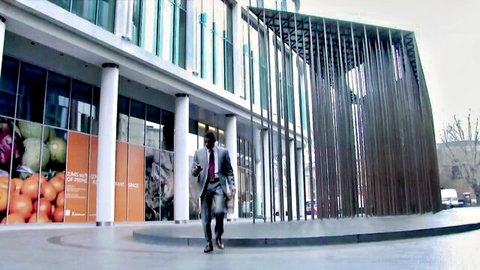 Businessman in gray suit walking past modern glass building with orange fruit posters