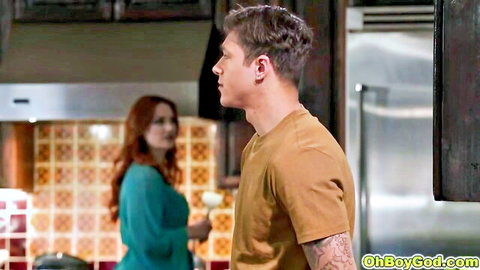 Redhead woman in teal dress holds glass beside tattooed guy in kitchen