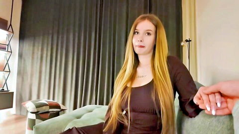 Long-haired blonde in tight maroon top holding hand intimately on green couch