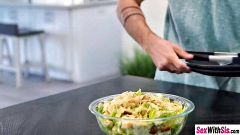 Tattooed man's hand holding black plates next to bowl of chickpea salad in kitchen