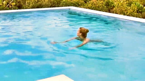 Redhead woman floating in outdoor pool in blue swimsuit, teasing relaxation