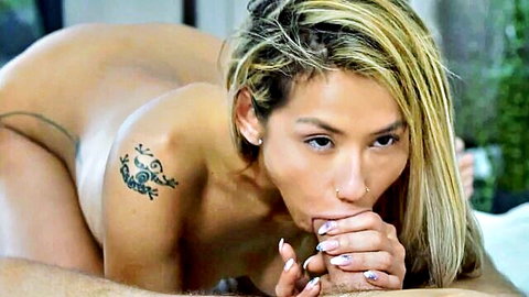 Tattooed blonde Asian with big ass nude on bed grips thick cock with nails pursed lips for POV blowjob