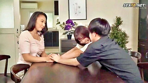 Smiling Japanese girls playfully grabbing Asian guy's hands at kitchen table tease