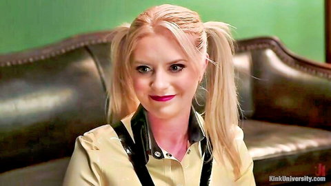 Blonde pigtail slut in shiny latex collar smiles seductively on couch