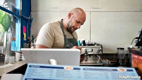 Muscular bald barista in apron preparing coffee for steamy cafe encounter