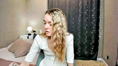 Skinny blonde teen webcam girl in tight white top smiling seductively on bed