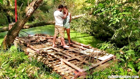 Beautiful girlfriend in short green dress embraces boyfriend on outdoor wooden bridge
