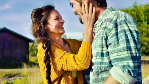 Brunette MILF in yellow sweater intimately touches bearded man's face outdoors near cabin