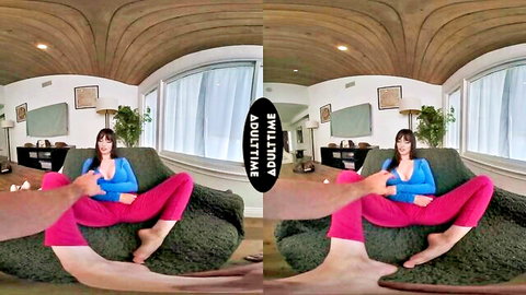 Lexi Luna in blue top and red pants teasing on couch with hand on thigh