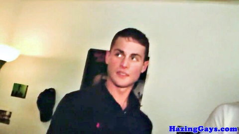 Handsome college guy in black polo shirt smiling in dorm for gay hazing.
