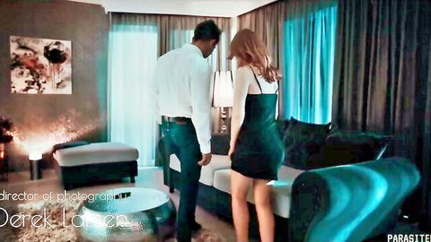 Redhead in tight black mini dress bends over showing ass to man in white shirt in luxury hotel room