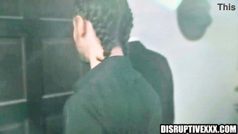 Man in suit with braided hair viewing screens in foster home scene