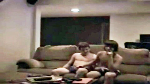 Shirtless Asian couple in shorts lounging intimately on couch