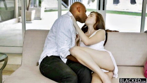 Interracial couple kissing passionately on couch in white dress