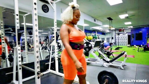 Curvy ebony babe in tight orange bra and shorts posing athletically in gym