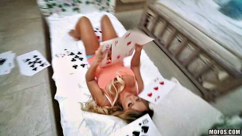 Blonde athletic spinner Cali Carter in orange top holding cards on bed