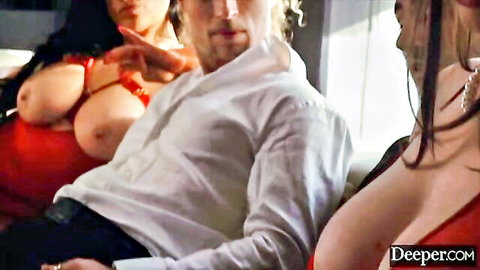 Two busty brunettes in red tops expose massive cleavage teasing man on couch
