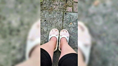 Closeup of sexy bare legs and feet in white Crocs sandals with pink bows on outdoor pavement