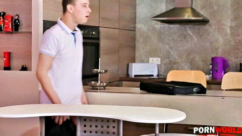 Surprised young guy grabbing crotch bulge over pants in modern kitchen