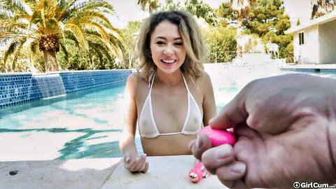 Petite blonde teen in tiny white bikini smiles as hand presses pink vibrator on her pussy by pool