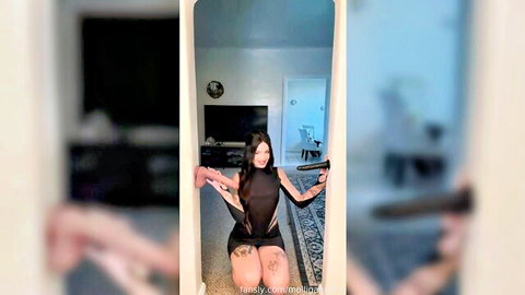 Julia Molligan posing seductively in black dress with two dildos