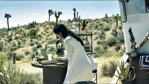 Sexy brunette in flowing white dress posing at desert table near RV with Joshua trees