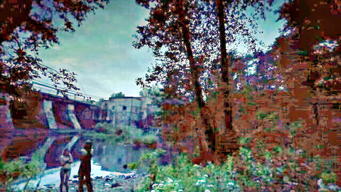 Clothed woman standing in shallow river near trees and old brick bridge in forest landscape
