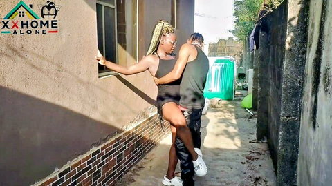 Braided ebony babe leans out window while muscular dude embraces her hips from behind in outdoor alley