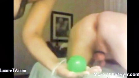Femdom woman holds green ball to insert into naked old man's exposed asshole with dangling cock and balls