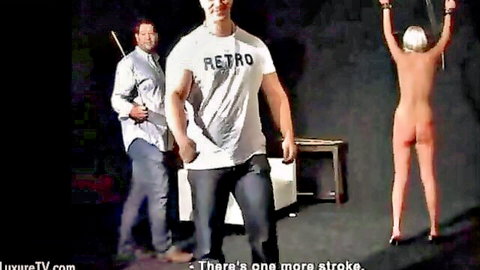 Nude blonde bound arms raised exposed ass as muscular Retro dom holds whip ready to strike in BDSM whipping