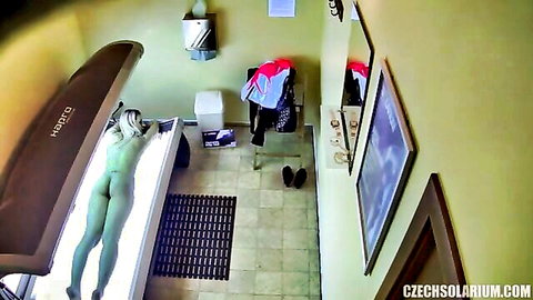 Naked blonde lying face down in solarium tanning bed exposing round ass and shaved pussy voyeur view