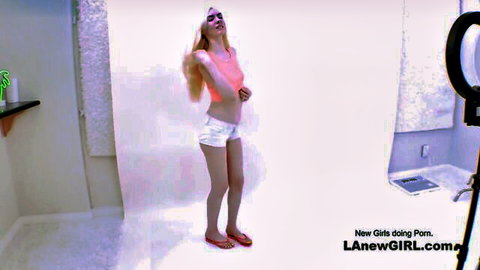 Cute blond babe in pink tank top and white shorts posing seductively