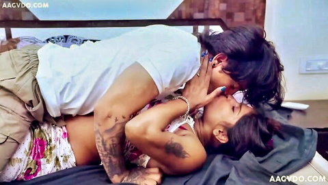 Tattooed South Asian couple passionately kissing on bed in steamy embrace