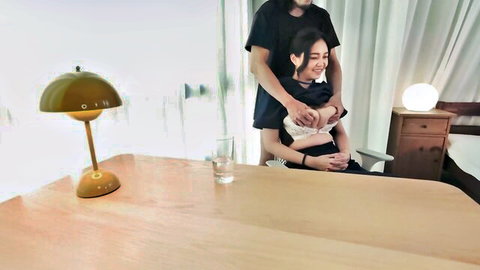 Smiling Asian girl hugged intimately by boyfriend hands on tits from behind at bedroom desk