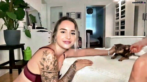 Tattooed blonde in red lace bra leans on bed petting cute chihuahua dog