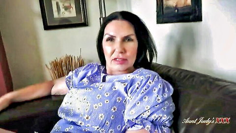 Mature brunette Aunt Judy smiling seductively in floral blue dress on couch