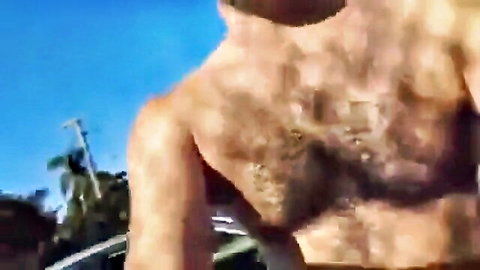 Sweaty hairy-chested young man shirtless outdoors in public with blue sky and palms