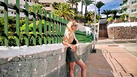 Blonde Mila in black bikini top and plaid mini skirt posing outdoors at sunny resort