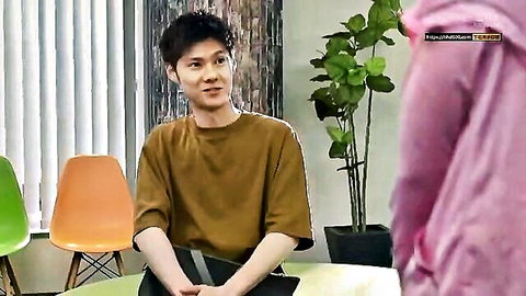 Handsome Asian man in beige t-shirt sitting smiling in modern studio with plants and chairs
