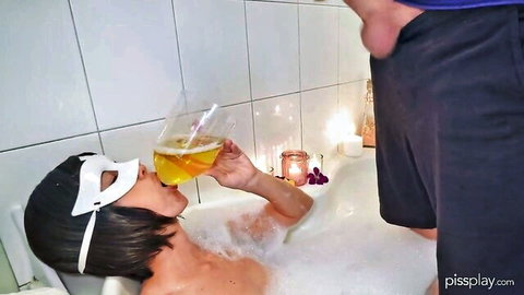 Masked woman in bubble bath sips champagne with erect cock inches from her face
