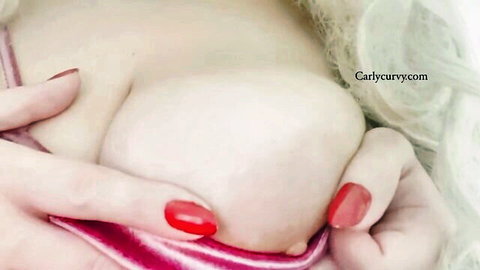 Close-up of large nude breast cupped by hands with red nails, blonde hair visible