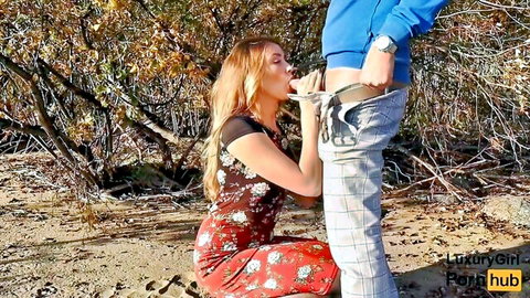 Blonde teen in floral dress gives outdoor blowjob on beach to standing man