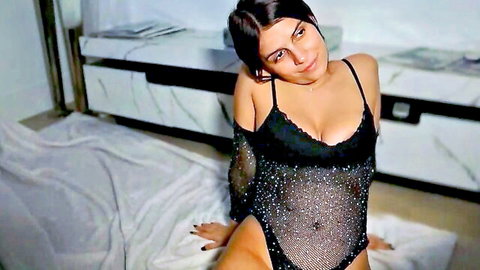 Brunette bombshell in sheer black sparkly mesh bodysuit teases with deep cleavage and thick thighs on floor