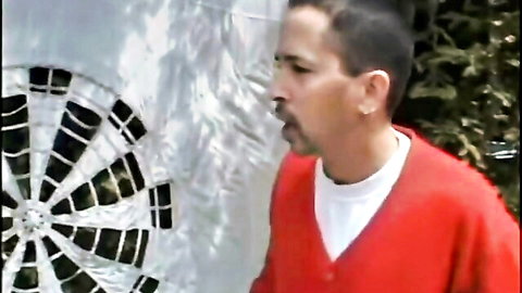 Man in red sweater and mustache aiming dart at outdoor dartboard.