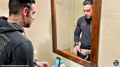 Tattooed muscular man in hoodie poses in bathroom mirror selfie