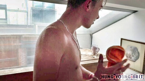 Shirtless muscular young man holds orange Fleshlight sex toy, sweaty skin glistening