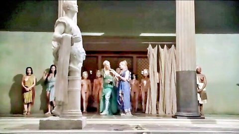 Scantily clad women surround nude male statues with visible cocks in ancient temple orgy setup
