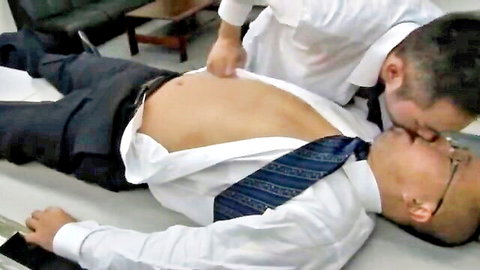 Gay suited men passionately kissing in office with open shirt exposing bare chest and abs